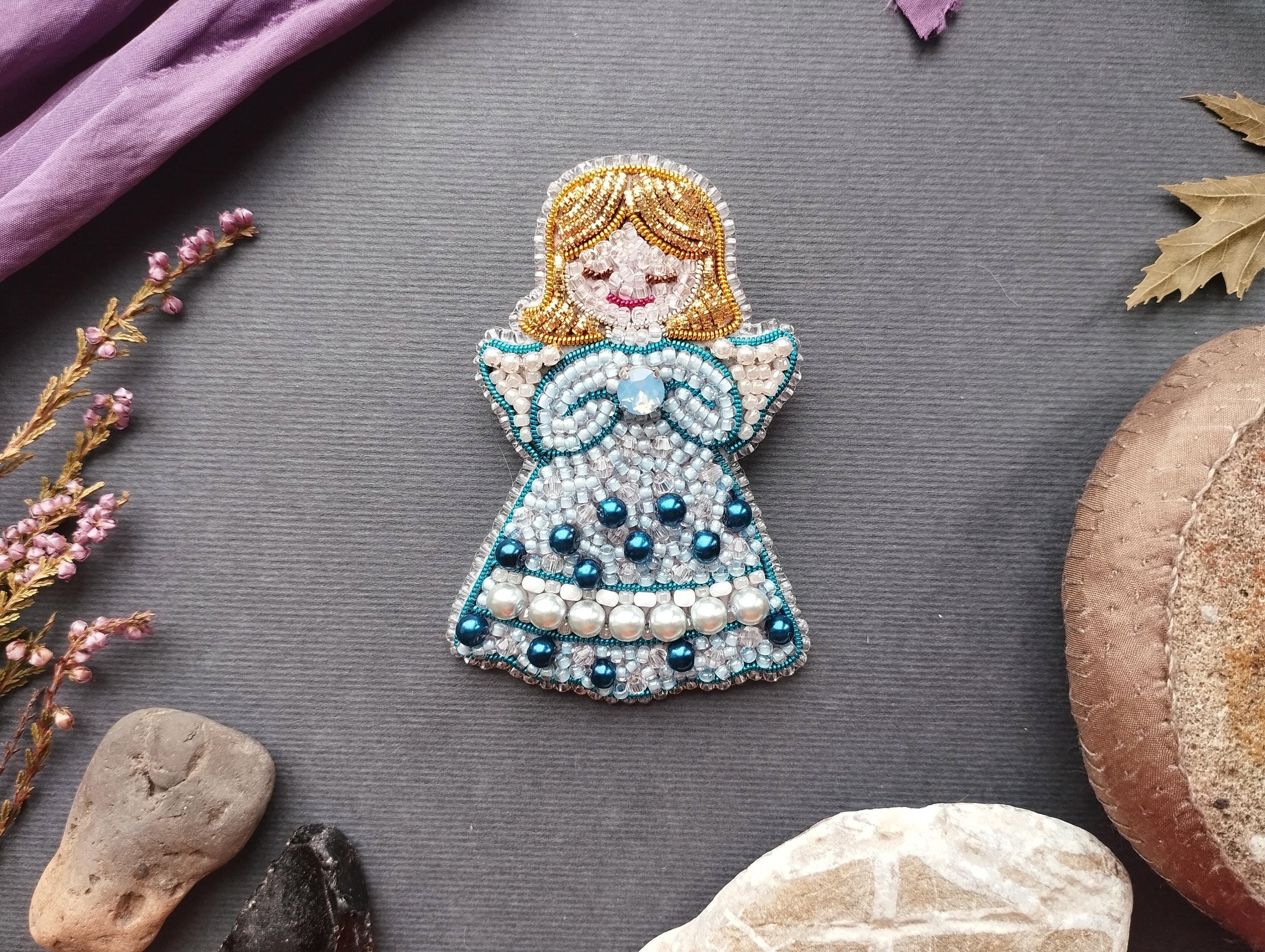a decorative piece of a girl with a blue dress and beaded details, surrounded by various natural elements such as flowers, rocks, and leaves.